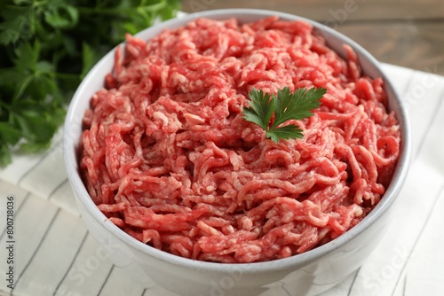 Raw ground meat in bowl and parsley on table, closeup