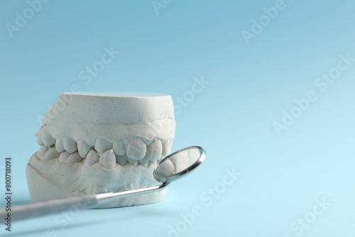 Dental model with gums and dentist mirror on light blue background, space for text. Cast of teeth photo
