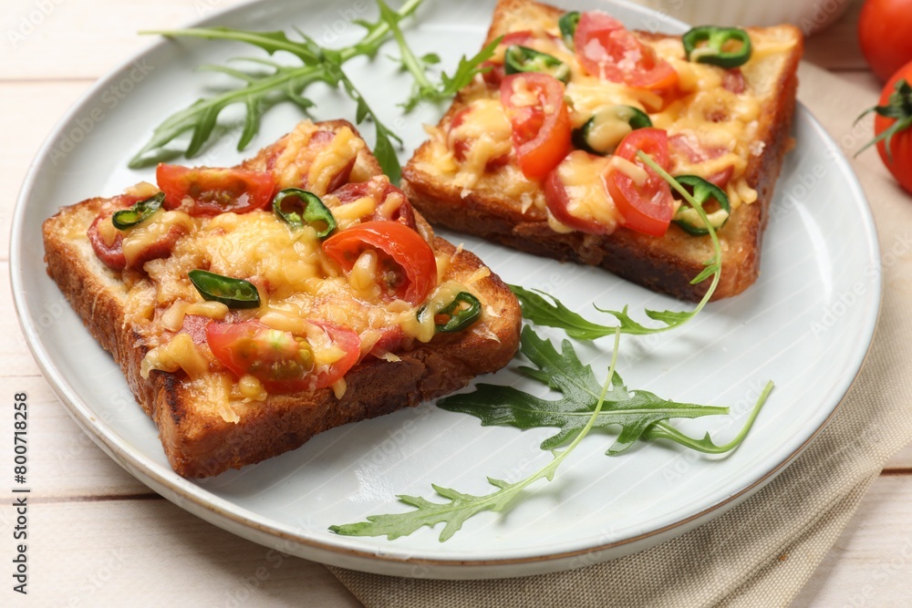 Tasty pizza toasts and fresh arugula on light wooden table, closeup