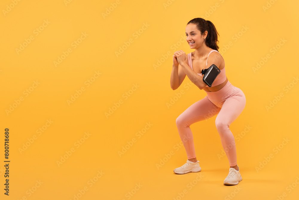 Fototapeta premium Young Woman Performing Squats Against a Vibrant Yellow Background