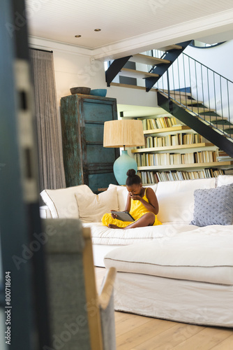 African American girl in yellow dress, reading at home on white couch photo