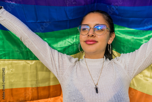 retrato de joven mujer con gafas alegre con la bandera del orgullo gay a su espalda  photo