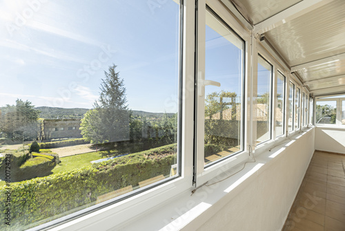 A closed terrace with large aluminum and glass windows with good views of the mountains with trees on a bright day