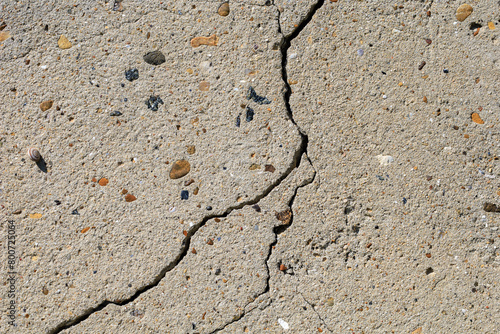 A cracked concrete surface with pebbles and rocks scattered across it