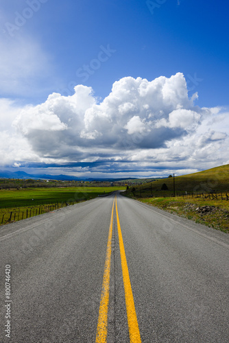 Two lane empty road in Eastern Oregon with double yellow lines leading to big clouds above distant horizon