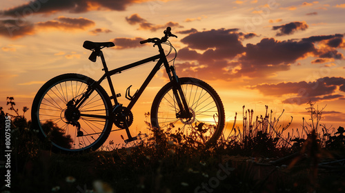 A bicycle is parked in a field with a beautiful sunset in the background. The bike is the only object in the scene, and it is a peaceful and serene moment captured in time