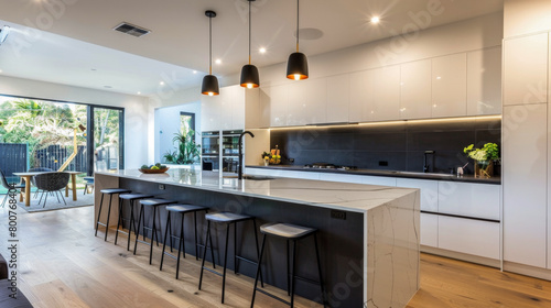 A large kitchen with a white counter and black stools. The kitchen is well lit and has a modern feel