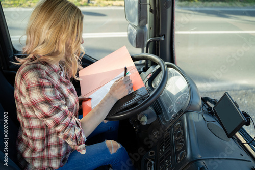 Woman truck driver filling up paperwork , on steering wheel 