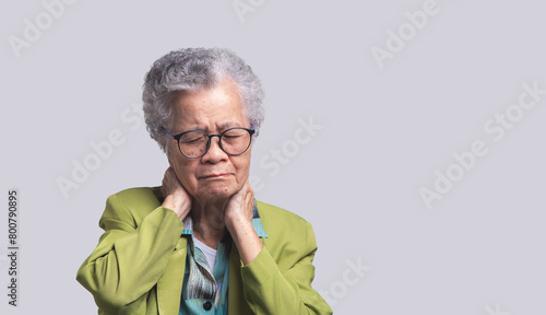 Senior woman suffering from neck pain stands on a gray background.