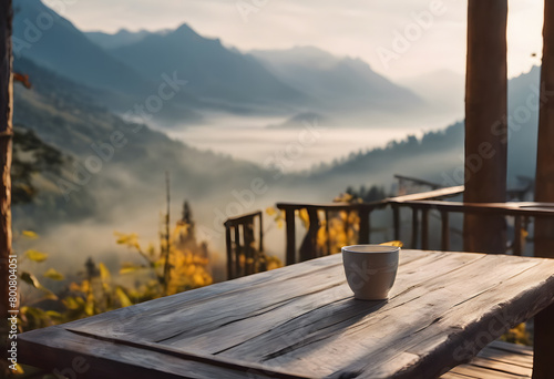 A serene morning view from a wooden deck featuring a cup of coffee, overlooking misty mountains and a forest.
