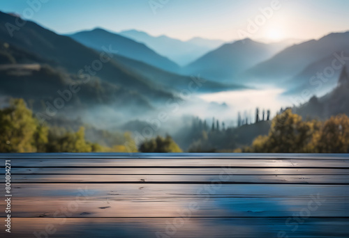 Misty mountain landscape viewed from a wooden deck at sunrise, with layers of hills and light fog.