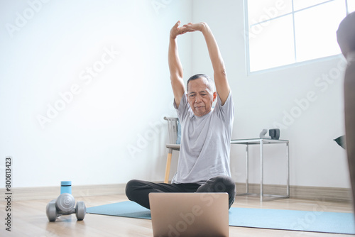 Senior Healthy Man Stretching Hands, Warming Up Before Workout at Yoga Mat with Online Instructor at Home 