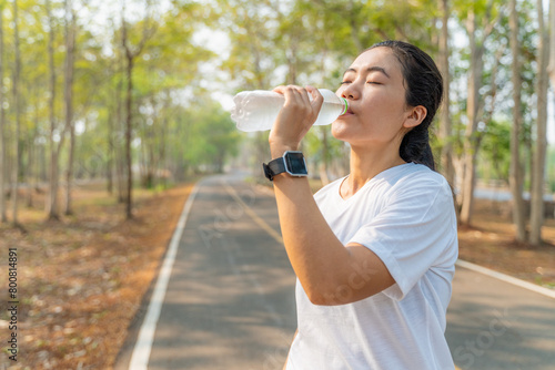 Young woman drinking water from a plastic bottle after her morning run at a local running park