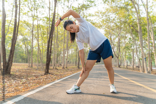 Young female runner stretching her arms and legs before starting her morning run at a local running park