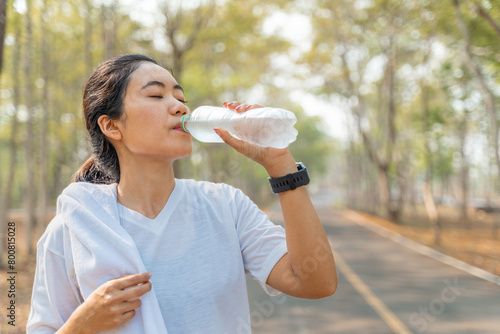 Young woman drinking water from a plastic bottle after her morning run at a local running park