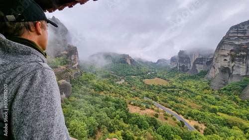 Selected focus on man with panoramic view of Holy Orthodox Monastery of Rousanou (St. Barbara), Kalambaka, Meteora, Thessaly, Greece, Europe. Rock formations surrounded by mystical dramatic fog photo