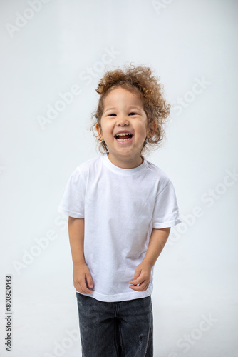 Curly mischievous girl, rejoicing, smiling, looking at the camera, in dark jeans posing on a white background