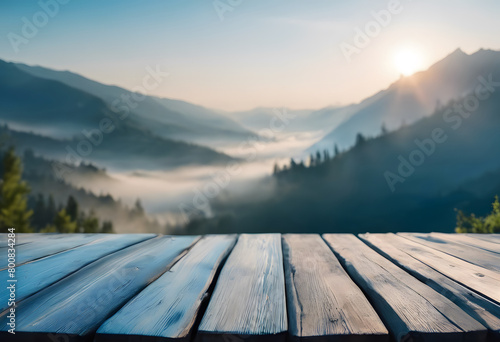 Sunrise over a misty mountain valley viewed from a wooden deck, showcasing layers of hills and a soft, glowing sky. © Tetlak