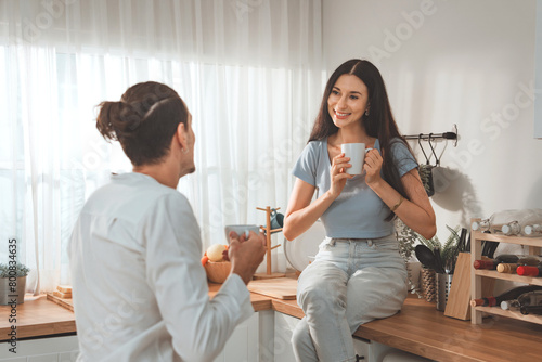 Married couple drinking cups of coffee together while resting seated on top table in kitchen at home, Man and woman enjoy pleasant conversation and beverage in morning, relations, love © oatawa