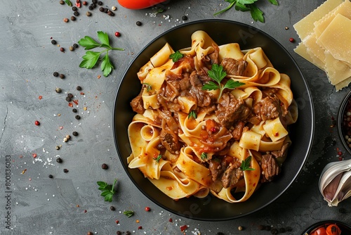 Close up of black bowl with beef ragout on pappardelle on grey background