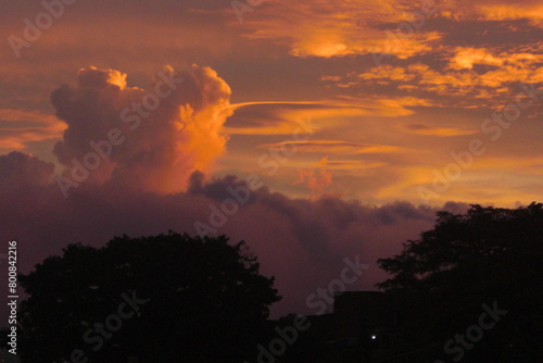 Atardecer con reflejo color naranja en las nubes. Silueta oscura de una casa y arboles. photo