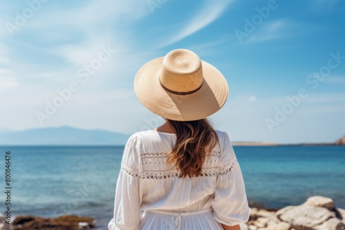 Woman in White Dress and Hat Looking Out at the Ocean. Generative AI © Uliana