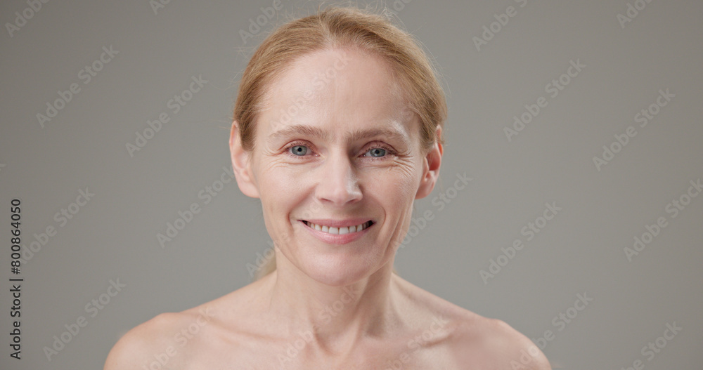 Anti age, Beauty, health and dry skin care concept - beautiful middle-aged mature Caucasian woman in her 50s touching her face skin and looking at the camera with a slight smile