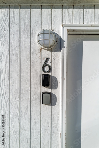 Exterior entrance to room number six in a white wood building with a doorframe and a lamp