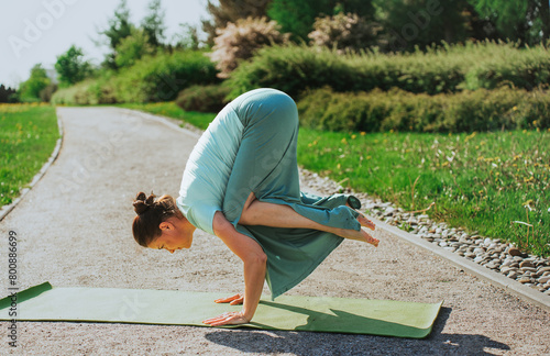 Woman practicing yoga in park, crow pose, concentration.