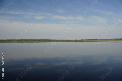 Lake in the forest. Water surface, open spaces and horizon. Blue sky. Reflection.