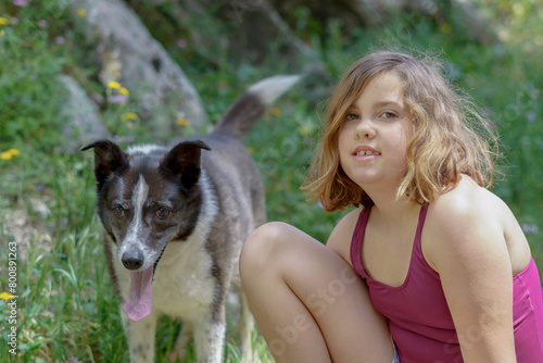 beautiful eight-year-old girl in red swimsuit playing with her border collie dog in the field