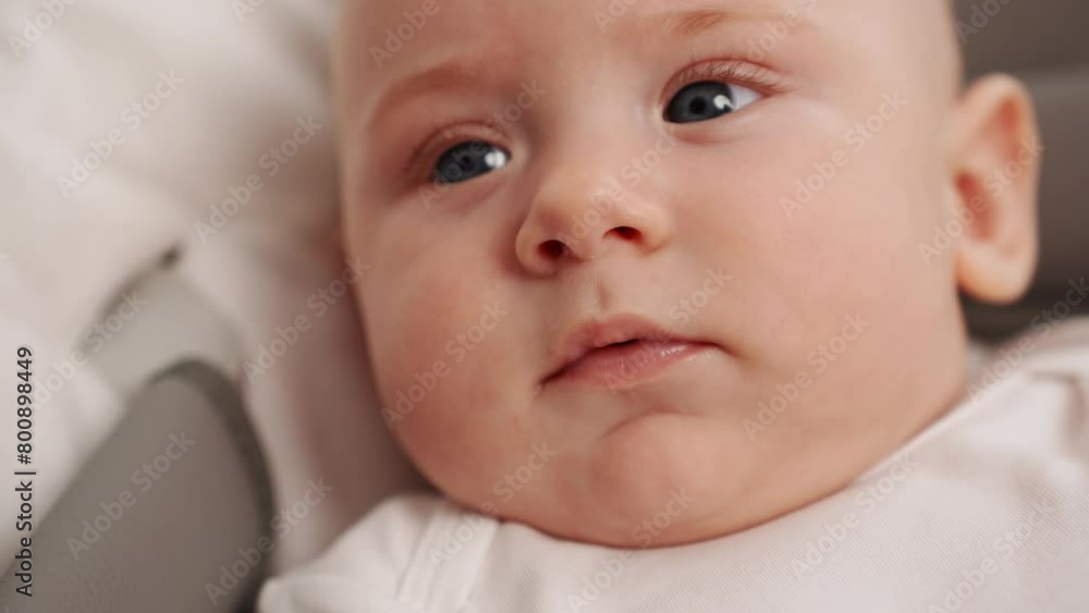 Cute infant lies in cocoon of a baby lounger, looks at camera, smiles, close-up. Portrait of blue-eyed newborn baby. Concept of maternity leave, child care, happy carefree childhood Cute infant lies in cocoon of a baby lounger, looks at camera, smiles, close-up. Portrait of blue-eyed newborn baby. Concept of maternity leave, child care, happy carefree childhood