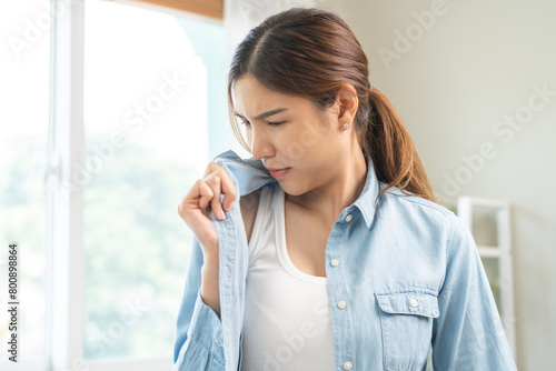 Bad smell nose concept asian young housewife woman having smelling clothes her shirt collar, sniff smelly dirty stinky musty, look disgusting from clothes after washed, laundry out of machine at home. photo