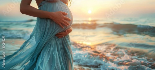 Pregnant woman in a blue dress on the beach at sunset photo