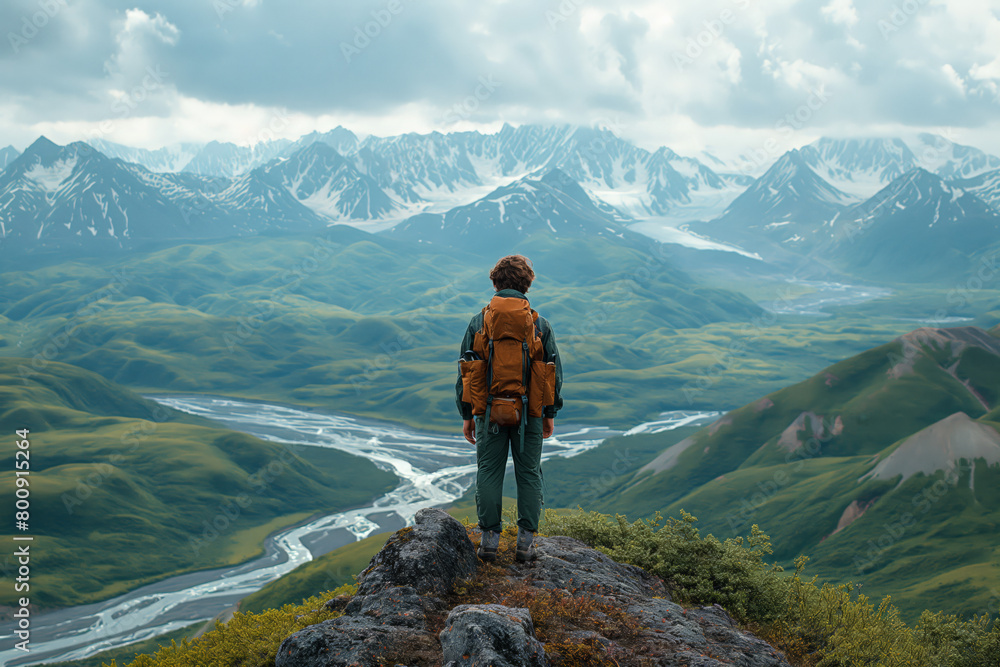 Hiker overlooking vast green valleys and snowy mountains