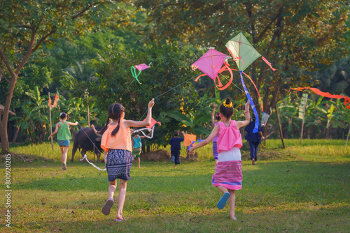 Foto Happy Asian Thai group of boys and girls wear traditional colorful farmer outfits and run with flying kites on a green field