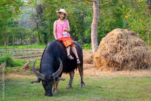 Beautiful Asian Thai females wear traditional farmer outfits and ride buffalo are happy to practice farming learn about the life of farmers. © pomphotothailand