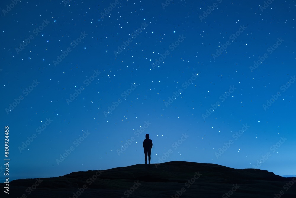 A lone figure standing on a hill, gazing up at the stars with wonder and awe, their silhouette a stark contrast against the deep blue, Generative AI