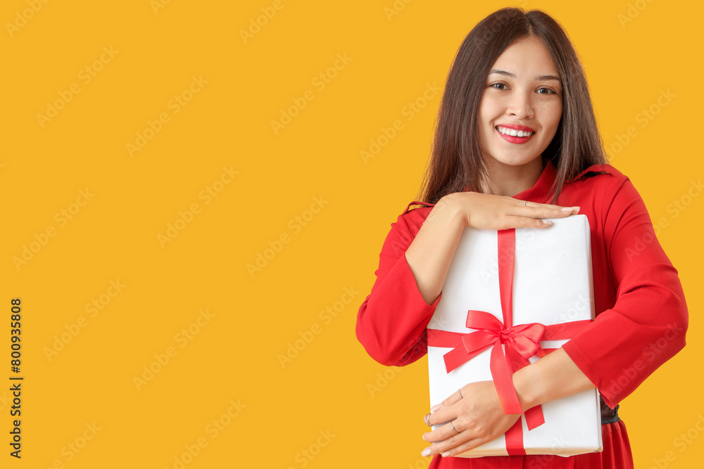 Beautiful young Asian woman with gift box on yellow background Beautiful young Asian woman with gift box on yellow background