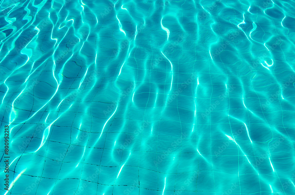 Waves on the light of the pool water. Swimming pool with blue water. Water surface texture. View from above.
