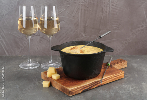 Fondue pot with tasty melted cheese, forks, bread and wine on grey table
