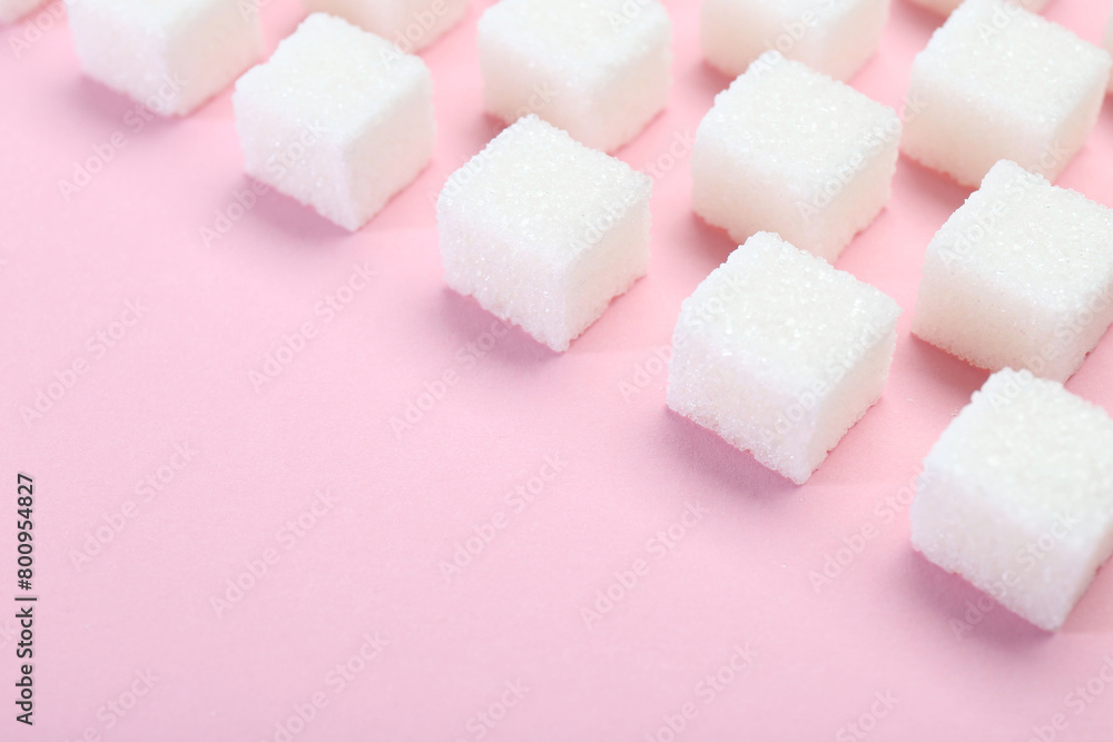 White sugar cubes on pink background, closeup. Space for text