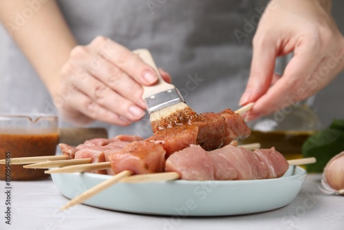 Woman spreading marinade onto raw meat with basting brush at table, closeup