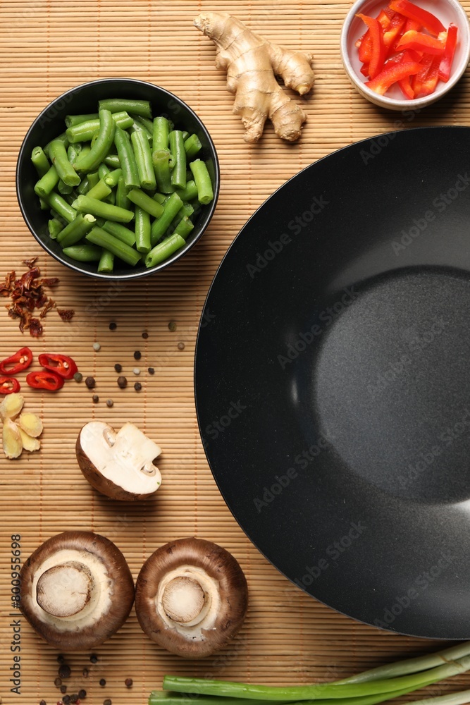 Flat lay composition with black wok, spices and products on bamboo mat