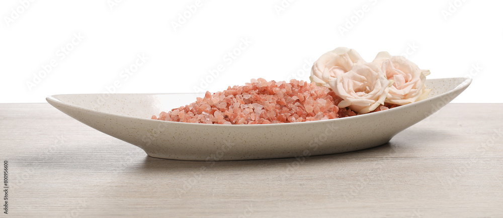 Natural sea salt in bowl and roses on light wooden table against white background Natural sea salt in bowl and roses on light wooden table against white background