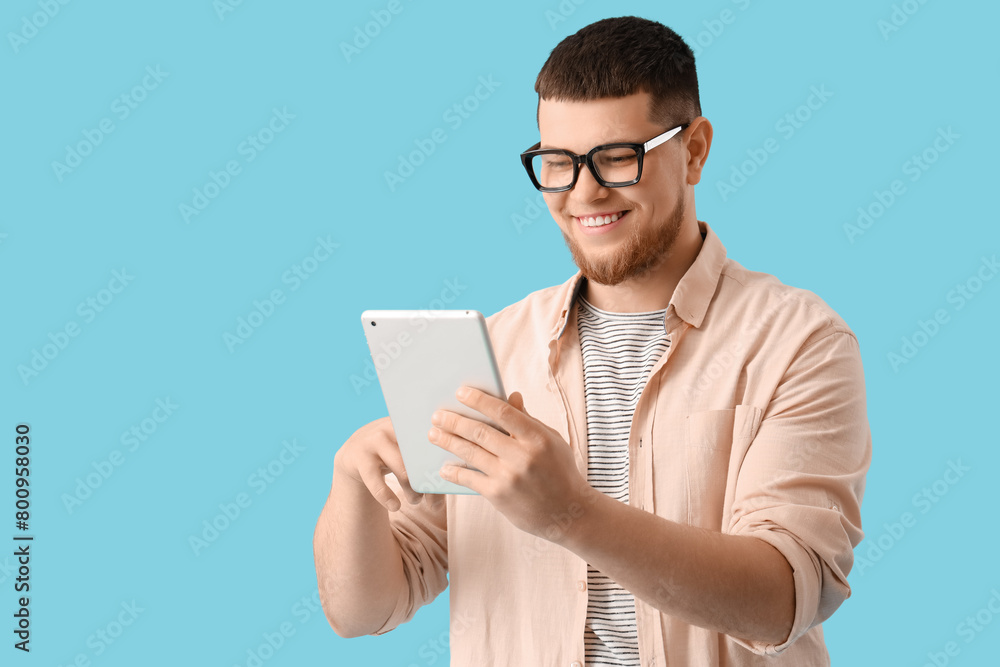 Young man in eyeglasses using tablet computer on blue background Young man in eyeglasses using tablet computer on blue background