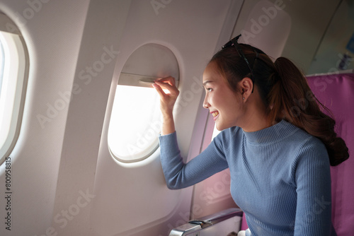 Asian female tourist sits smiling, opens window, admires the view, clouds float in the sky by the window, happy on her trip abroad. travel concept.
