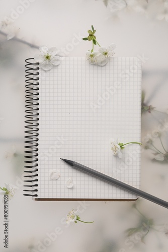 Guest list. Notebook, pencil and beautiful cherry tree blossoms on spring floral background, flat lay