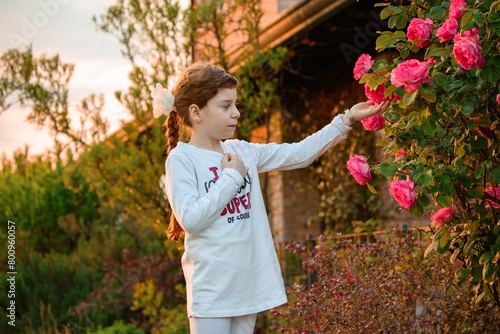 Bambina con capelli lunghi che accarezza e mostra fioritura di rose. Foto per comunicazione pubblicitaria, marketing e business