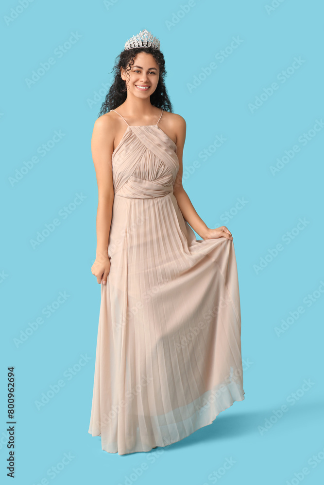 Beautiful young African-American woman in stylish prom dress and tiara on blue background Beautiful young African-American woman in stylish prom dress and tiara on blue background